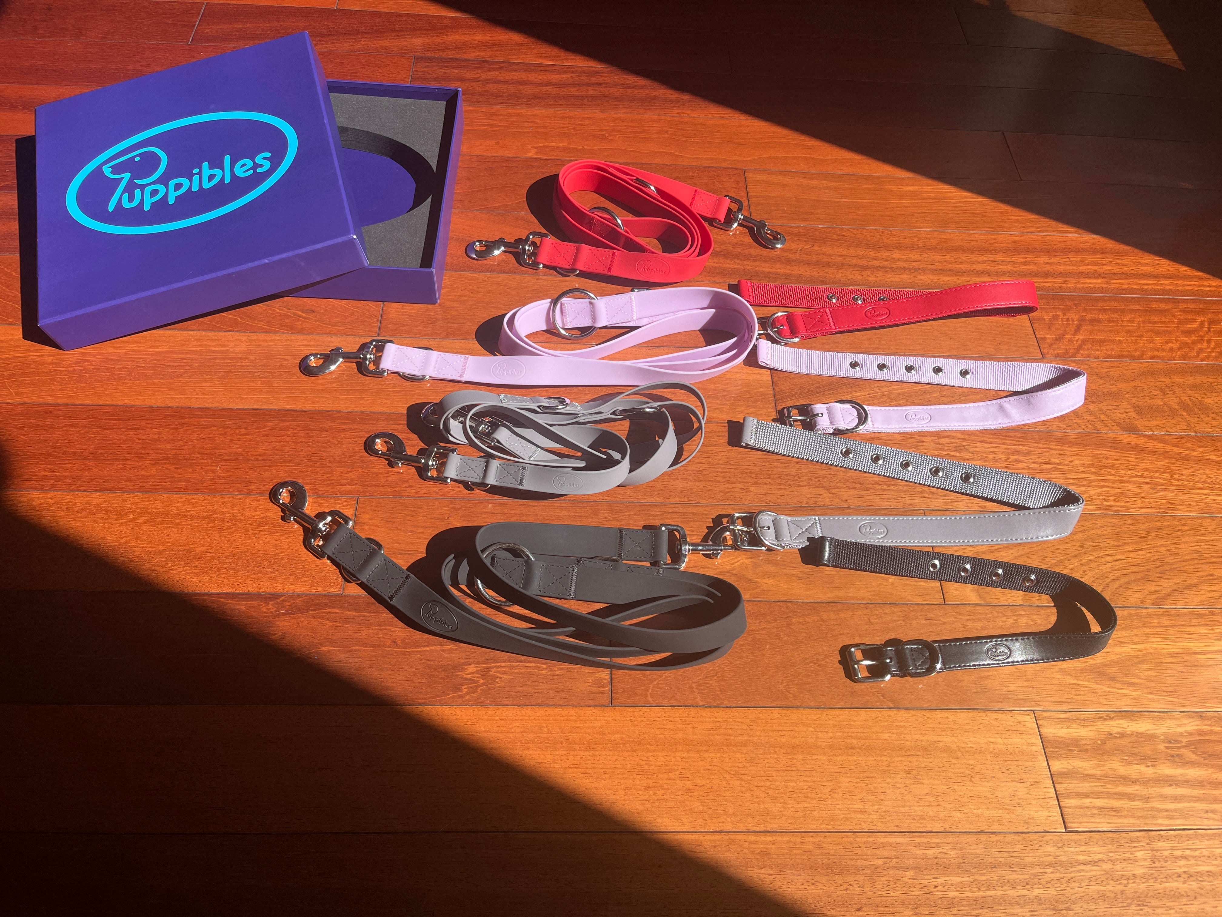 Black, grey, lavender, red collars and leashes next to box bearing Puppibles logo